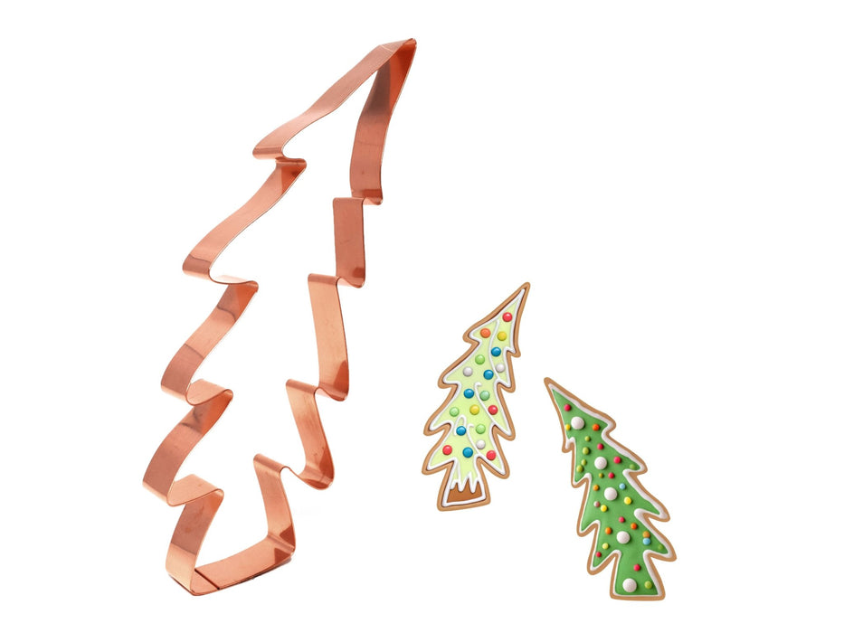 Copper Christmas tree cookie cutter with two decorated cookies on a white background