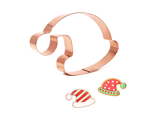 Copper cookie cutter shaped like a Santa hat with two cut-out hats on a white background
