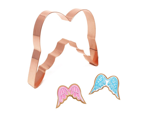 Copper angel wing cookie cutter with two cookies shaped like wings on a white background