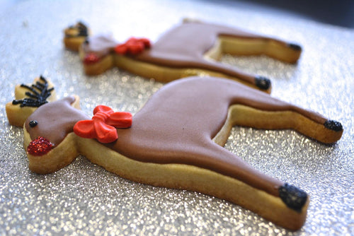 Festive reindeer-shaped Christmas cookies decorated with brown icing, red bows, and glitter details, showcasing The Fussy Pup’s Christmas collection of cookie cutters and holiday baking tools.