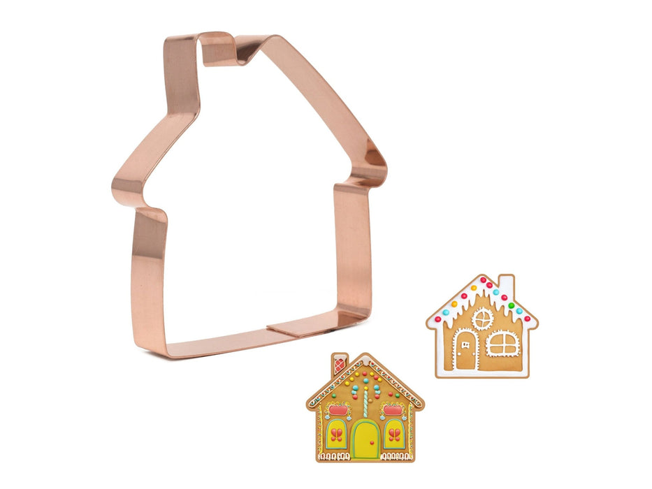 Copper house-shaped cookie cutter with two gingerbread house illustrations on a white background