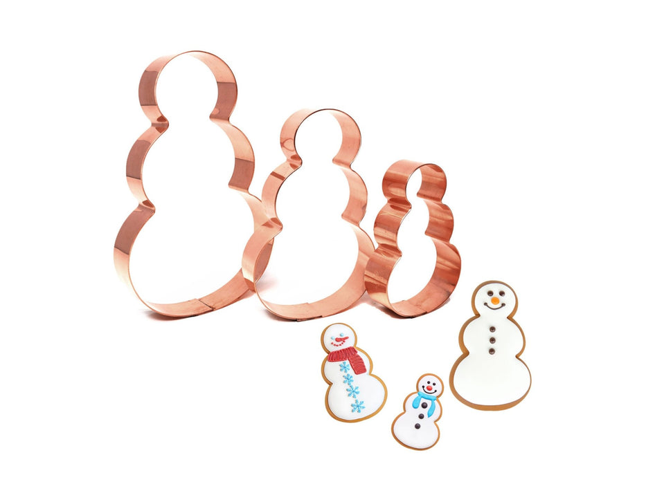 Set of copper snowman-shaped cookie cutters with snowmen cookies on a white background